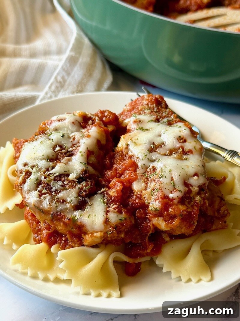 25-Minute Chicken Parmesan Recipe for Busy Family Dinners 12 Chicken parmesan plated over cooked pasta on a serving dish with a fork.