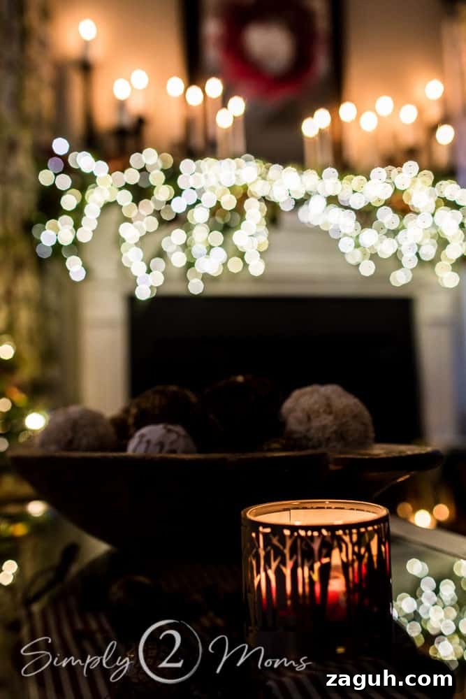 Classic Christmas Candlelight Tour You Have to See This Year 12 coffee table with fireplace mantle decorated with lush Christmas garland embellished with red berries, eucalyptus leaves, and magnolia leaves with white tapers and pillar candles on black candlesticks in background
