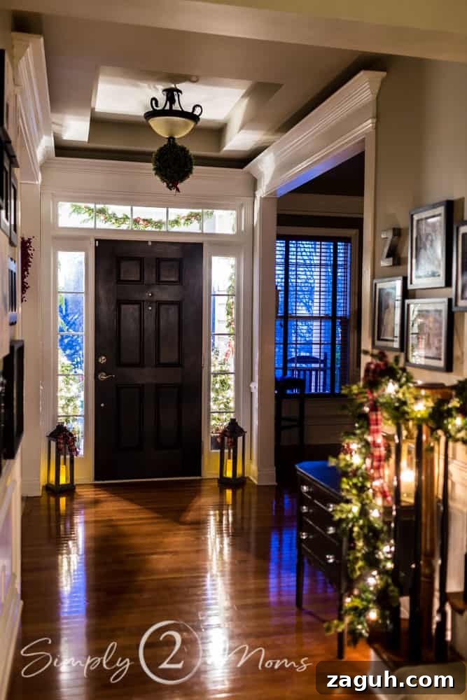 Classic Christmas Candlelight Tour You Have to See This Year 13 foyer decorated for Christmas with lanterns, kissing ball, lighted garland, gallery wall, black interior door