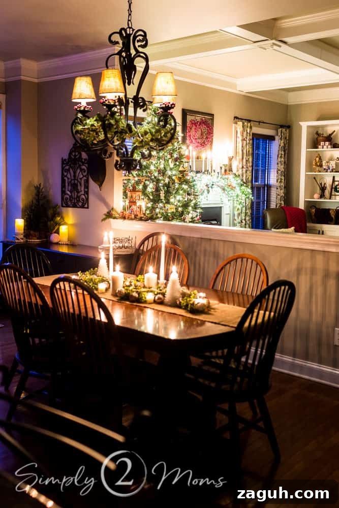 Classic Christmas Candlelight Tour You Have to See This Year 16 view of kitchen table with Christmas centerpiece lit by candles, chandelier decorated with ivy and red berries, open concept with family room in background
