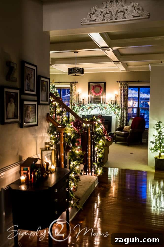 Classic Christmas Candlelight Tour You Have to See This Year 4 foyer with stairs decorated with lighted garland, nativity scene and view of family room with Christmas tree and lit fireplace decorated for Christmas with candle, greenery, and red berries