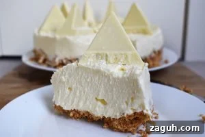 White Chocolate Toblerone Cheesecake Recipe — Creamy No-Bake Slice 2 Slice of White Chocolate Toblerone Cheesecake on a white plate on a wood board.