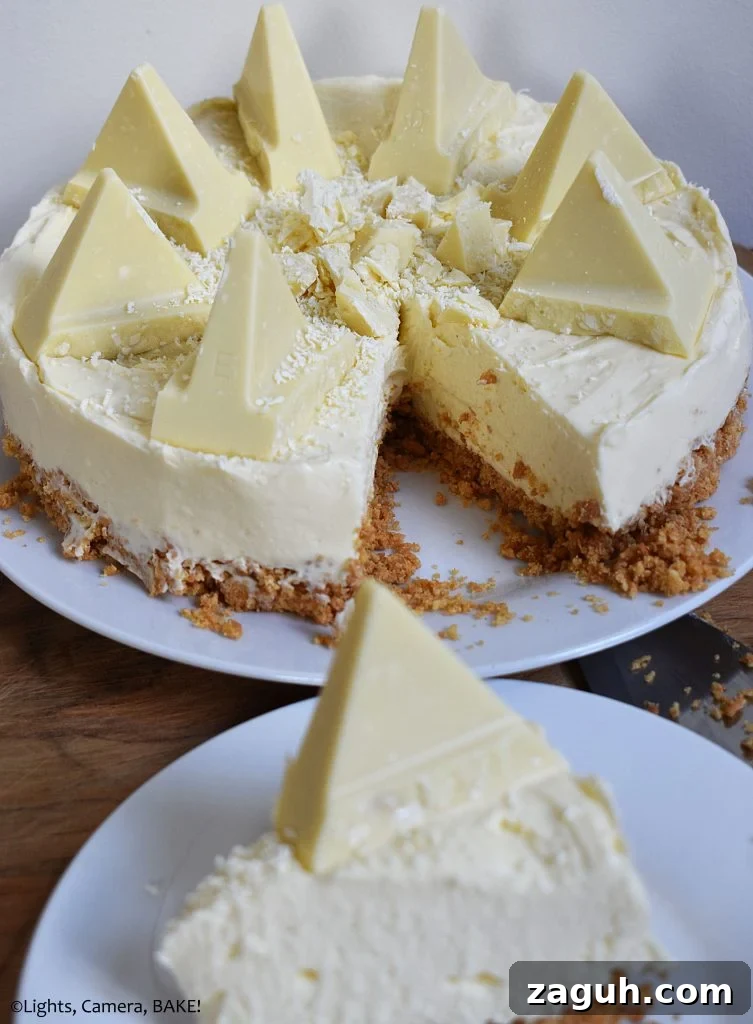 White Chocolate Toblerone Cheesecake Recipe — Creamy No-Bake Slice 3 Vertical view of a slice of White Chocolate Toblerone Cheesecake on a white plate with the full cheesecake in the background.