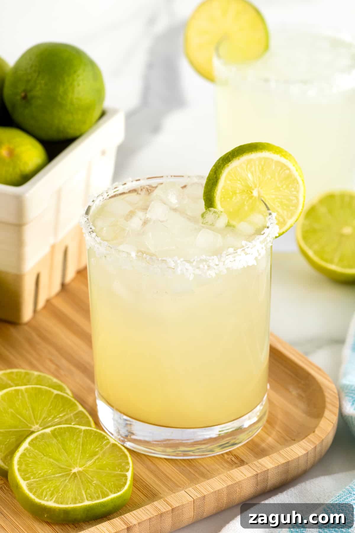 Authentic Mexican Fiesta Recipes for Your Party Menu 17 A salt rimmed glass filled with margarita on a rimmed wooden serving tray. There is a lime wedge on the rim of the glass.