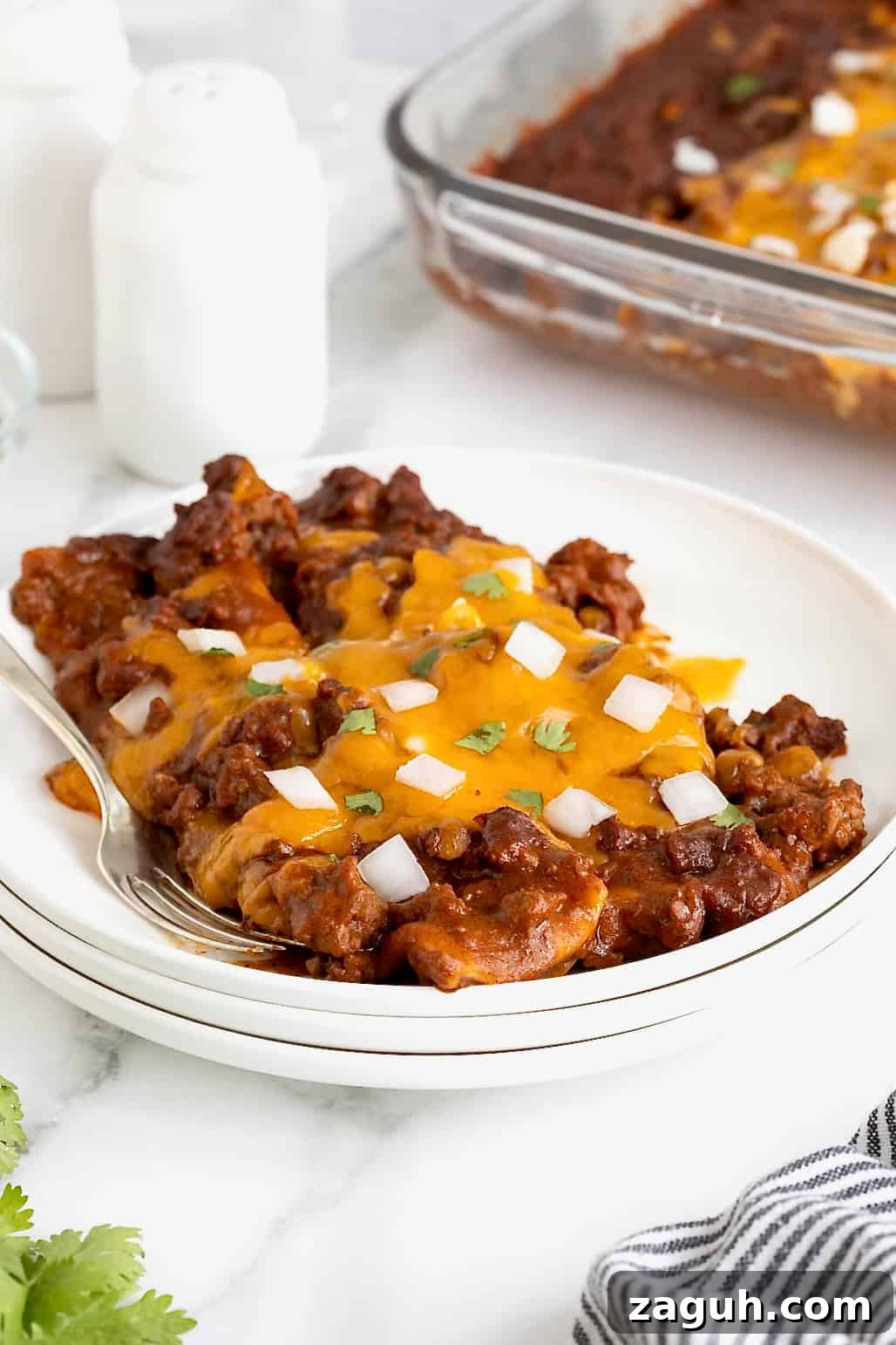 Authentic Mexican Fiesta Recipes for Your Party Menu 19 Three chili con carne enchiladas on a stack of three white plates.