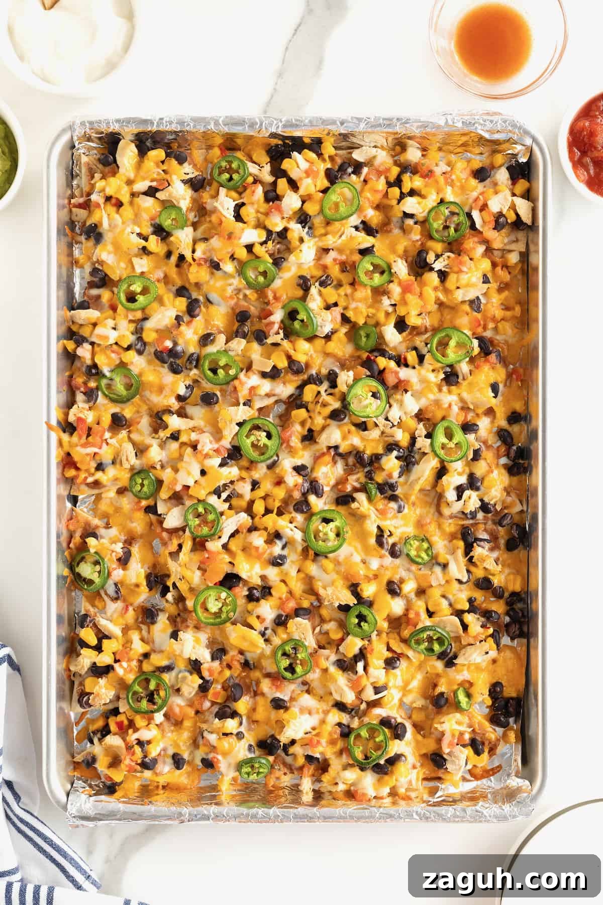 Authentic Mexican Fiesta Recipes for Your Party Menu 27 An aluminum sheet pan filled with nachos topped with cheese, black beans and jalapeño slices.