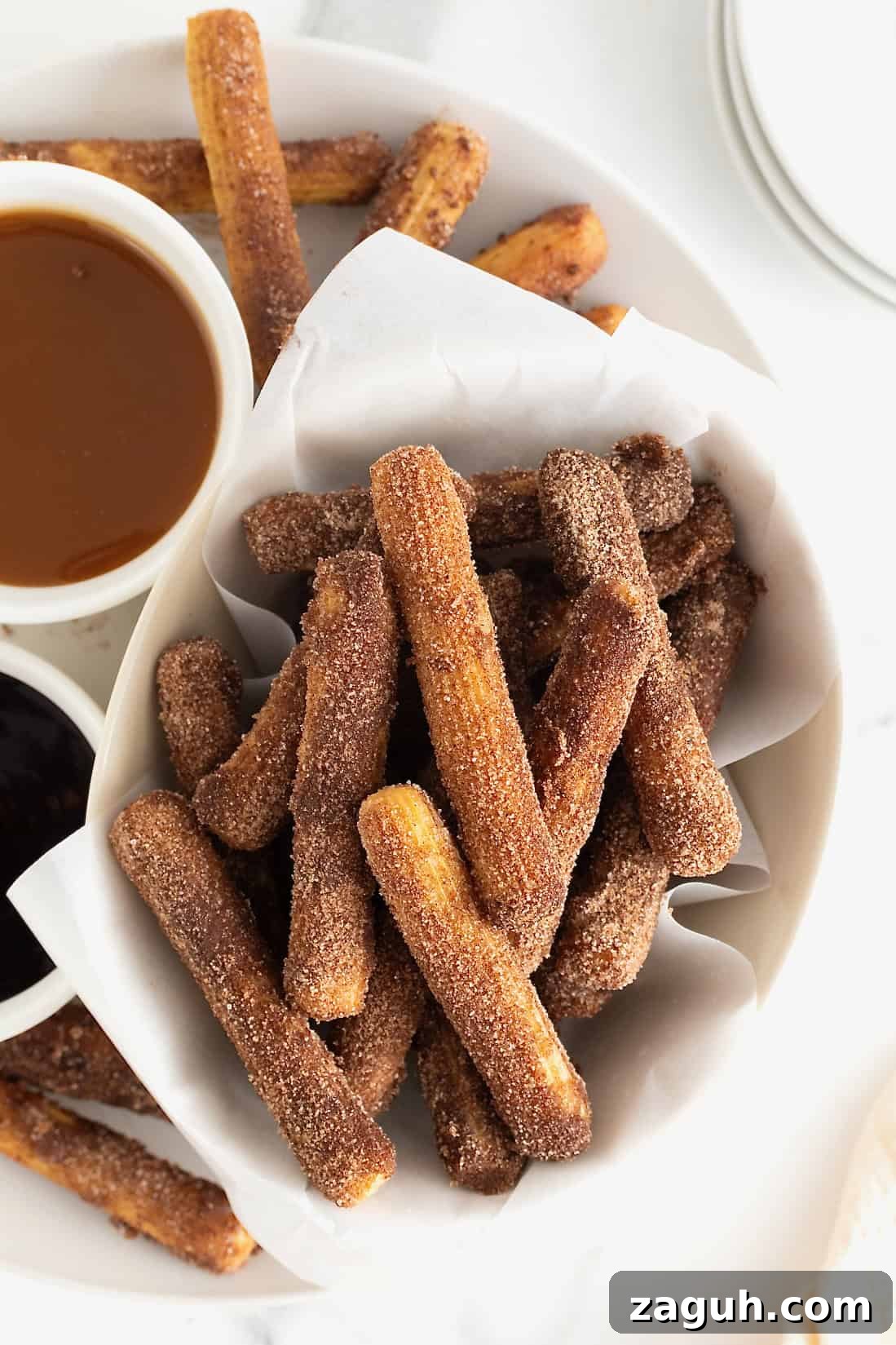 Authentic Mexican Fiesta Recipes for Your Party Menu 30 A parchment lined bowl of baked churros next to dipping sauces in white bowls.