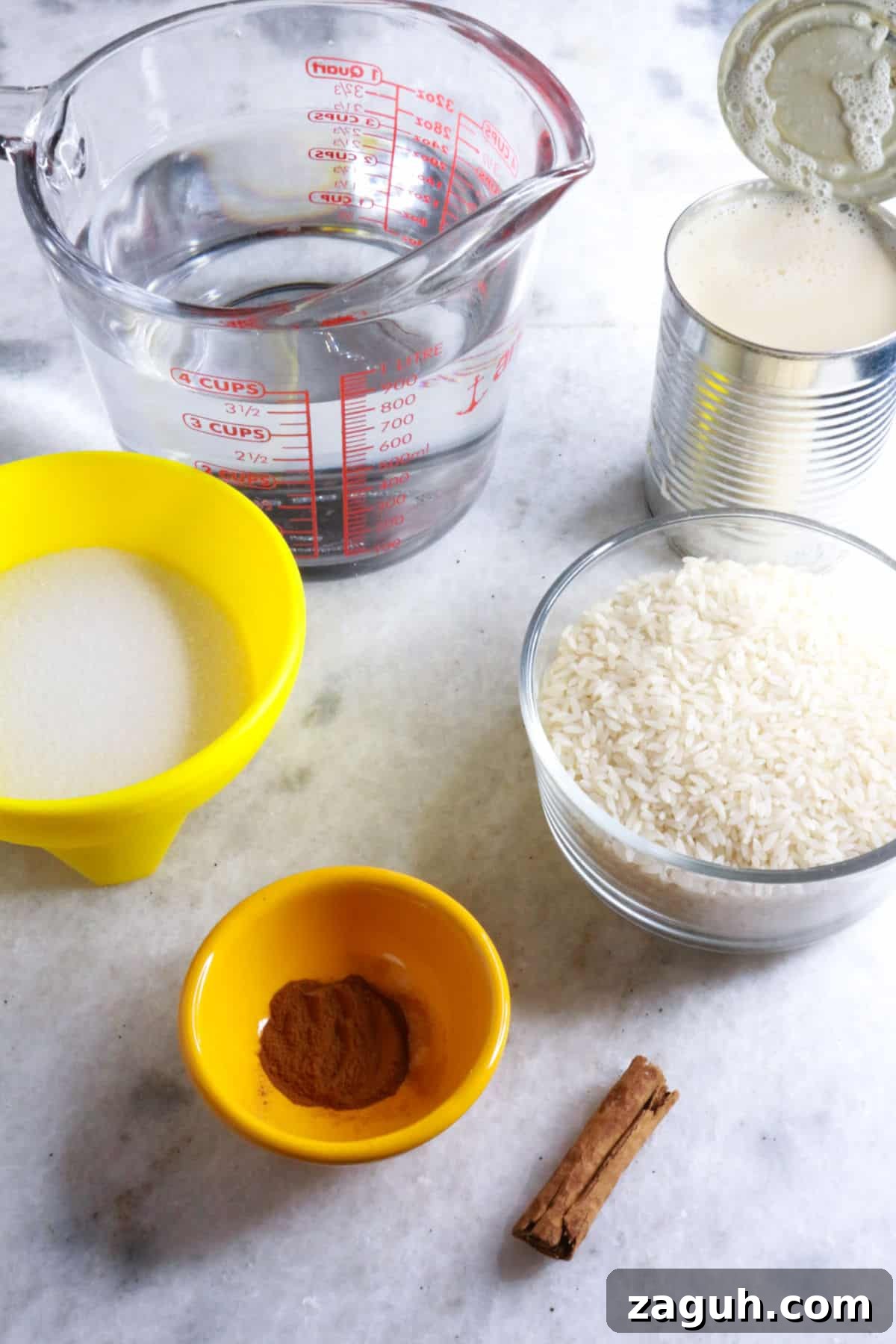 Refreshing Horchata Agua Fresca Recipe: Traditional Mexican Rice Drink 3 Measuring cup with water, can with evaporated milk, container with sugar, one with rice, another with ground cinnamon and a cinnamon stick