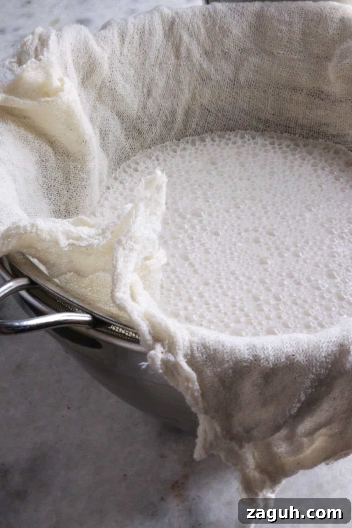 Refreshing Horchata Agua Fresca Recipe: Traditional Mexican Rice Drink 7 Cheesecloth on a strainer on top of a bowl filled with horchata