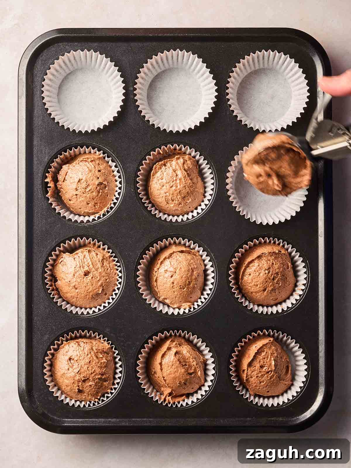 Decadent Chocolate Easter Cupcakes with Spring Decorations 7 A muffin tray on a white surface, with half of them filled with chocolate Easter cupcake batter.