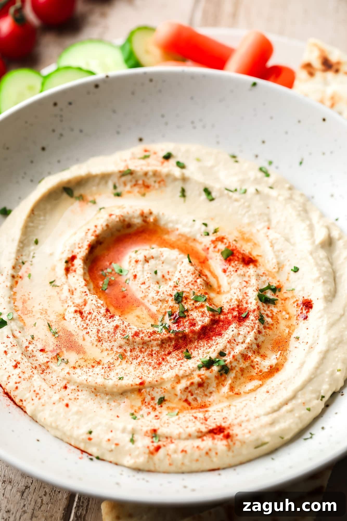 creamy hummus topped with paprika, herbs, and oil in a white bowl.