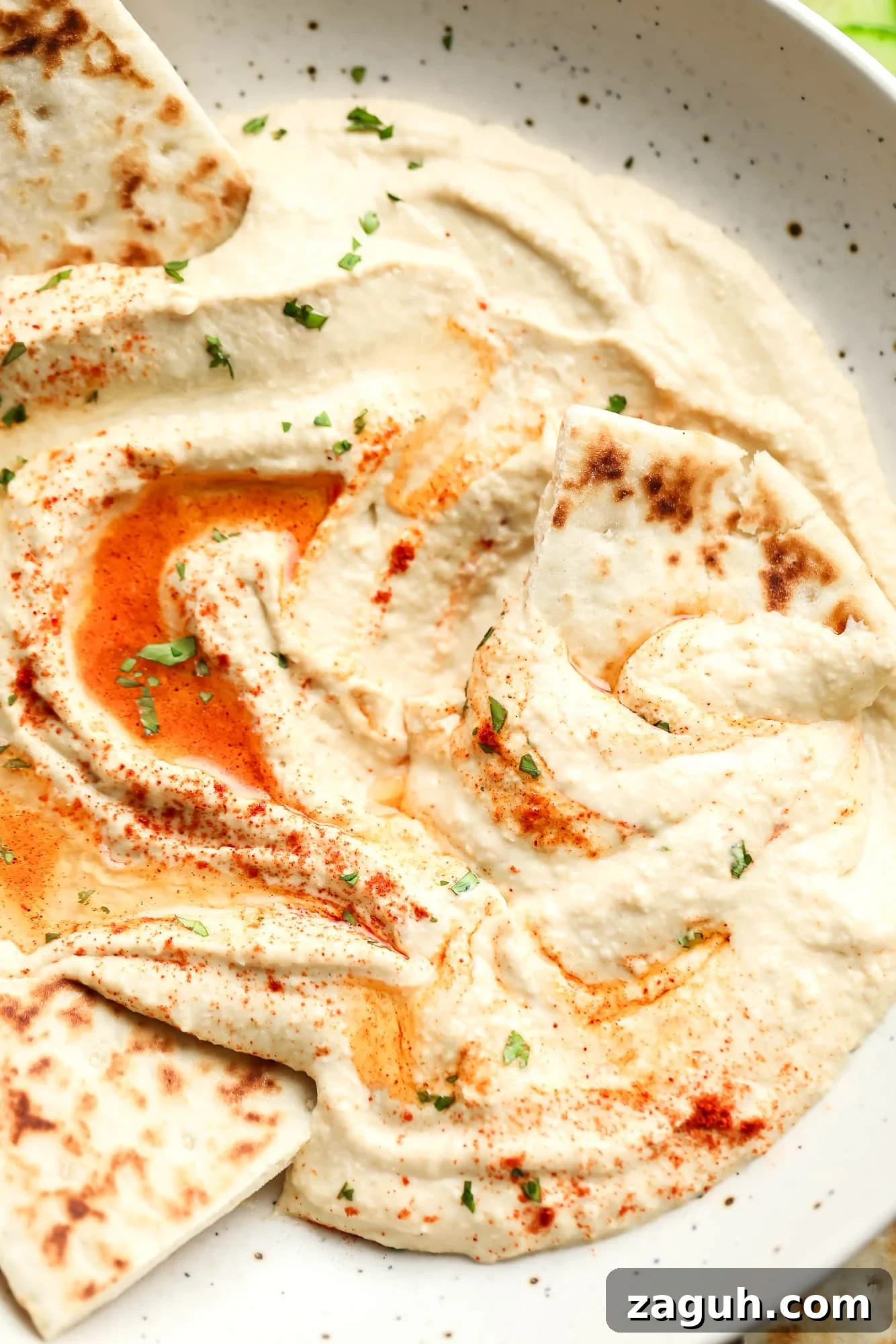 hummus topped with paprika and oil in a white bowl with pita bread on the side.