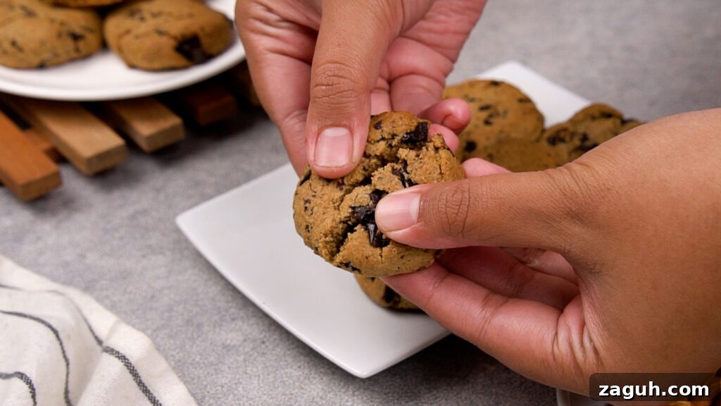 Almond Flour Chocolate Chip Cookie Recipe — Soft & Chewy</assistant 13 Hands gently breaking a freshly baked paleo chocolate chip cookie in half, showing the soft and gooey chocolate interior.