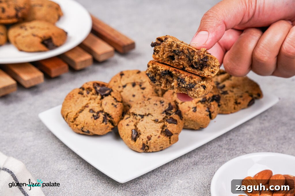 Almond Flour Chocolate Chip Cookie Recipe — Soft & Chewy</assistant 14 A hand breaking a paleo chocolate chip cookie in half, revealing the soft, gooey interior with melted chocolate.