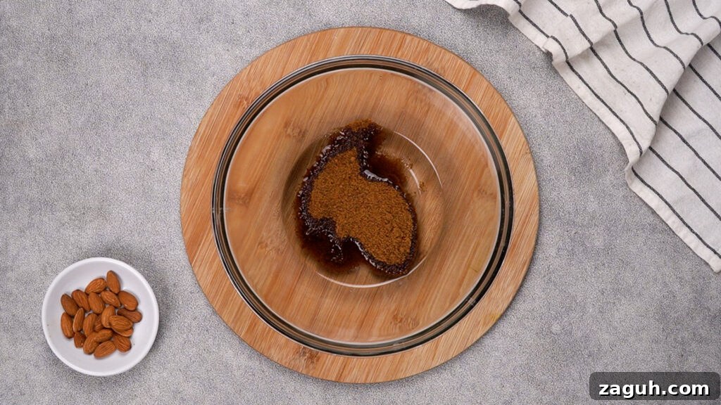 Almond Flour Chocolate Chip Cookie Recipe — Soft & Chewy</assistant 6 A glass mixing bowl on a wooden board containing coconut oil and coconut sugar at the start of the creaming process. A small bowl of whole almonds is placed nearby.