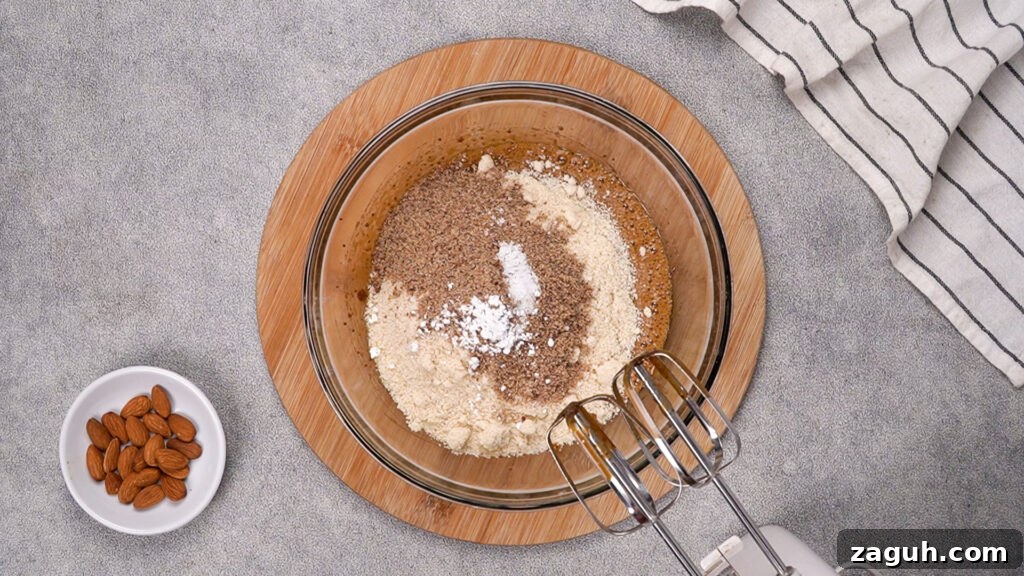Almond Flour Chocolate Chip Cookie Recipe — Soft & Chewy</assistant 7 The mixing bowl with added almond flour, flaxseed meal, salt, and baking soda on top of the wet mixture, ready to be combined with an electric mixer.