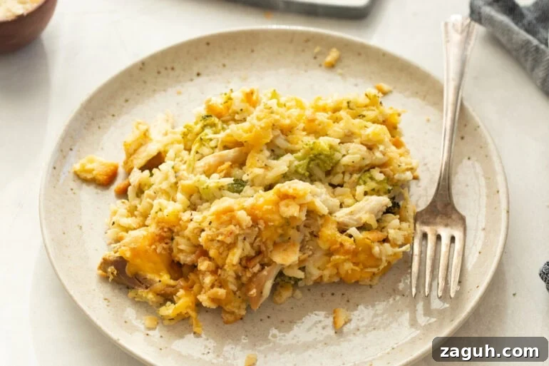 Simple Chicken, Broccoli and Rice Casserole Recipe 5 a dinner plate with a serving of cheesy chicken broccoli rice casserole on it with a fork sitting next to it