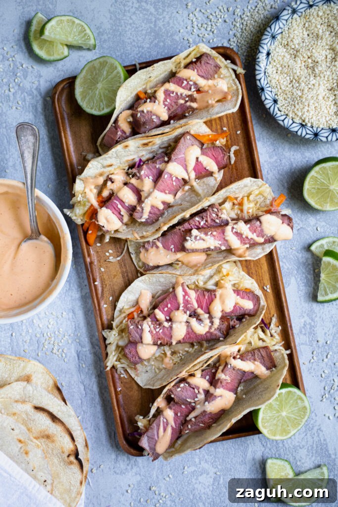 Grilled Tuna Steak Tacos with Crunchy Coleslaw 2 Five tuna steak tacos sitting on a string platter garnished with sriracha mayo and sesame seeds.