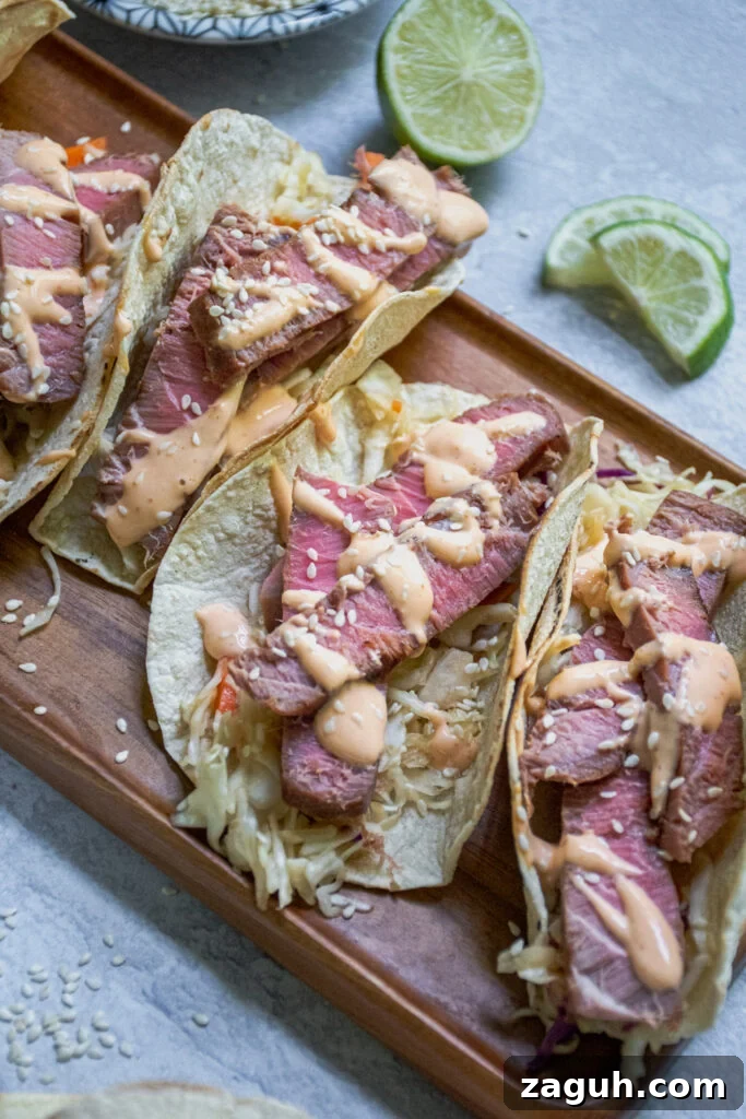 Grilled Tuna Steak Tacos with Crunchy Coleslaw 3 Angled view of the tuna steak tacos showing off the sliced tuna steak overtop a bed of coleslaw and topped with sriracha mayo and sesame seeds.