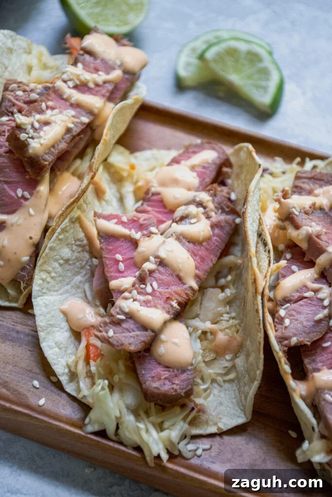 Grilled Tuna Steak Tacos with Crunchy Coleslaw 9 A side view of a close up of a tuna steak taco showing of slice tuna with pink middle garnished with sriracha mayo and sesame seeds.