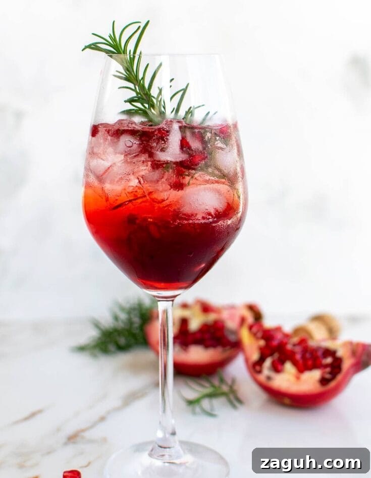 A pomegranate and campari spritz garnished with pomegranate seeds and rosemary.