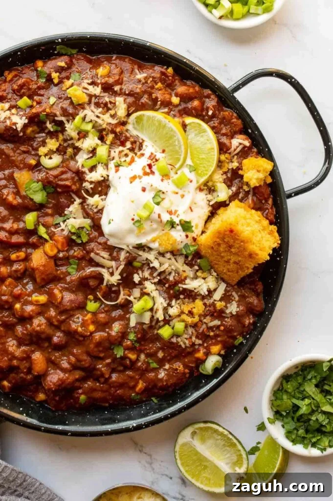 Guinness Vegan Chili Recipe: Rich, Hearty Stovetop Chili 8 Top-down view of a black pan with chili in it and herbs and limes to the side.