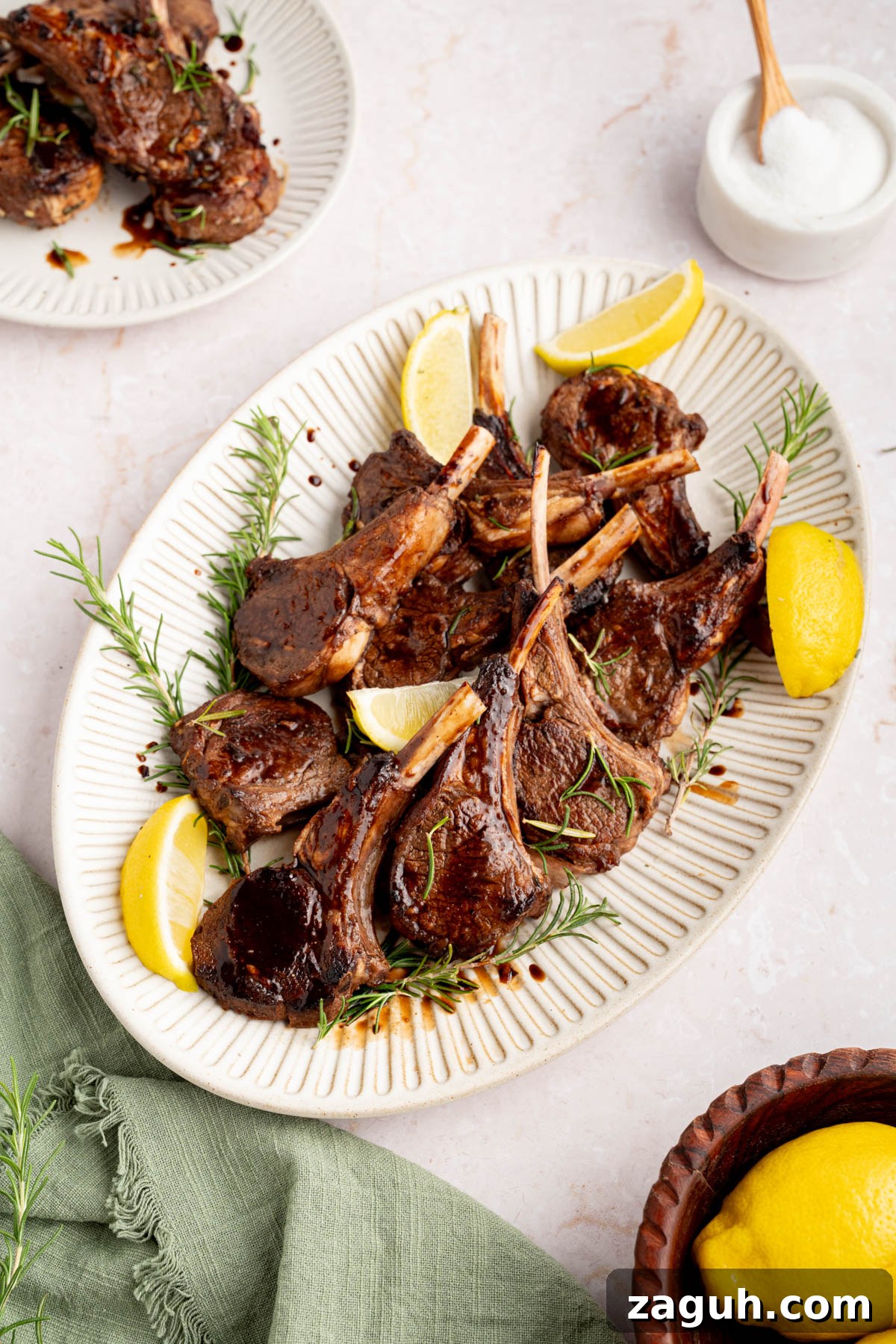 Balsamic-Glazed Oven-Baked Lamb Chops for Weeknight Dinner 9 The baked lamb chops with balsamic honey glaze on a white serving plate garnished with rosemary and lemon wedges.