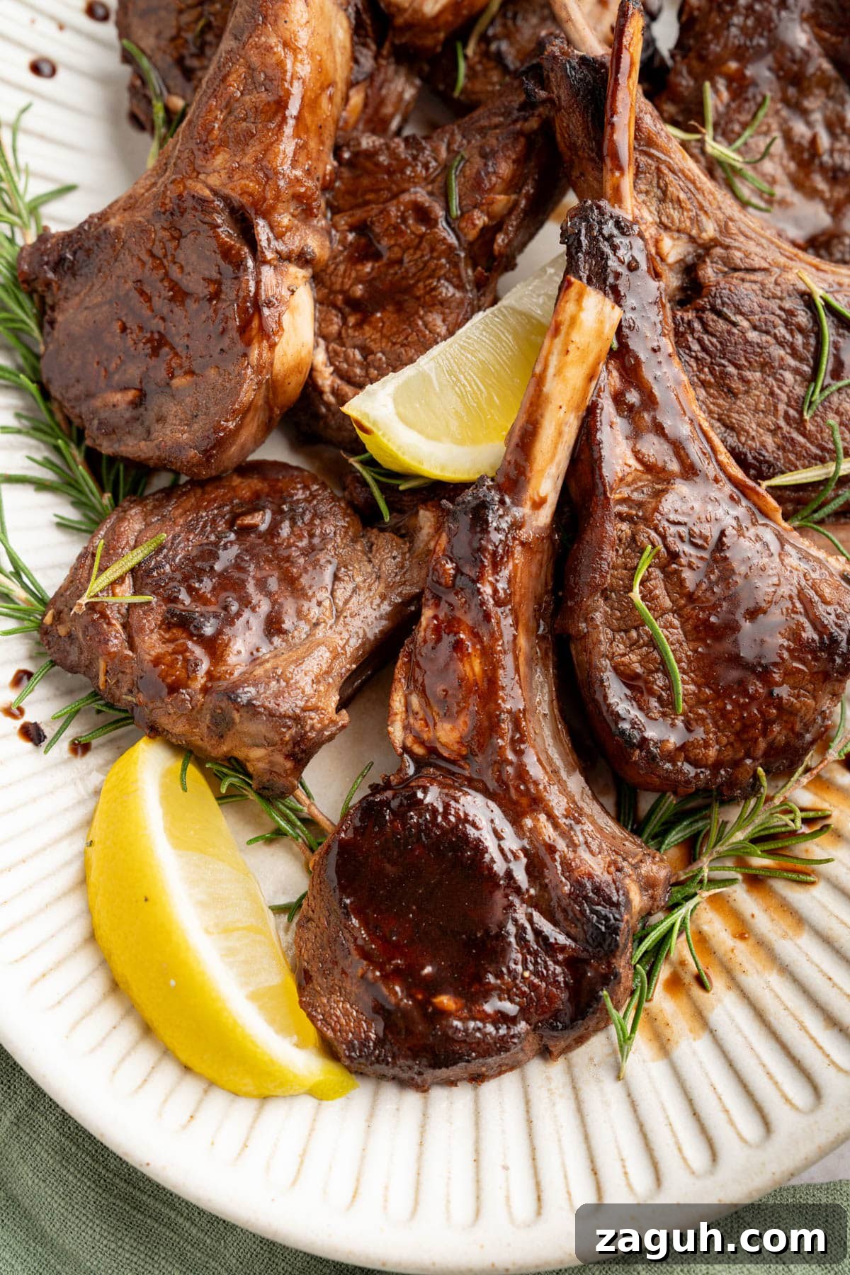 Balsamic-Glazed Oven-Baked Lamb Chops for Weeknight Dinner 10 Oven baked lamb chops with balsamic glaze on a serving platter garnished with fresh rosemary and lemon wedges.