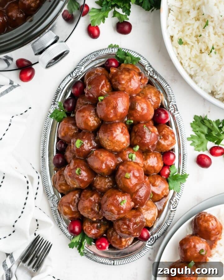 Cranberry meatballs on a oval silver platter with fresh cranberries and parsley around on the table.