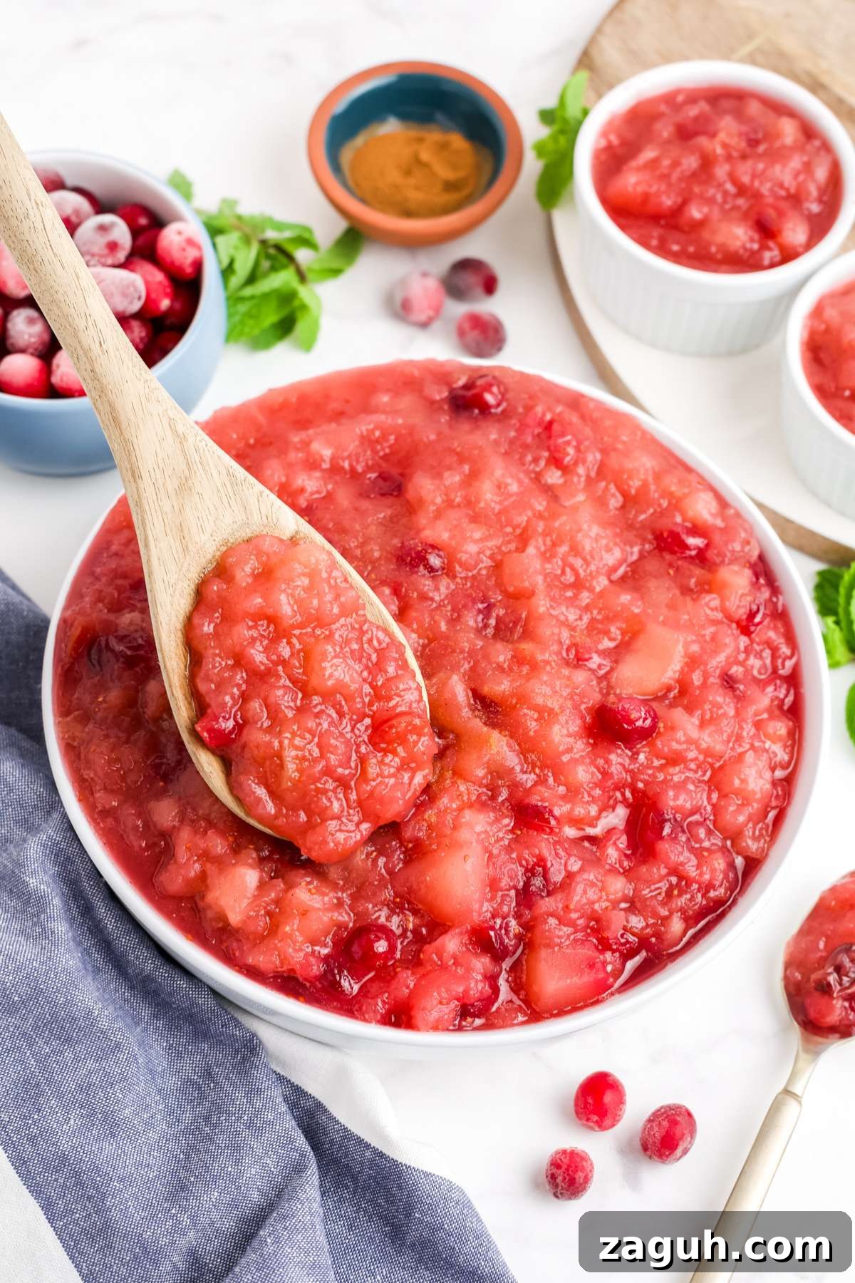 Cranberry Apple Sauce Recipe: Tangy Homemade Spread for Fall 7 Cranberry applesauce in a bowl with a wooden spoon held up over the bowl.