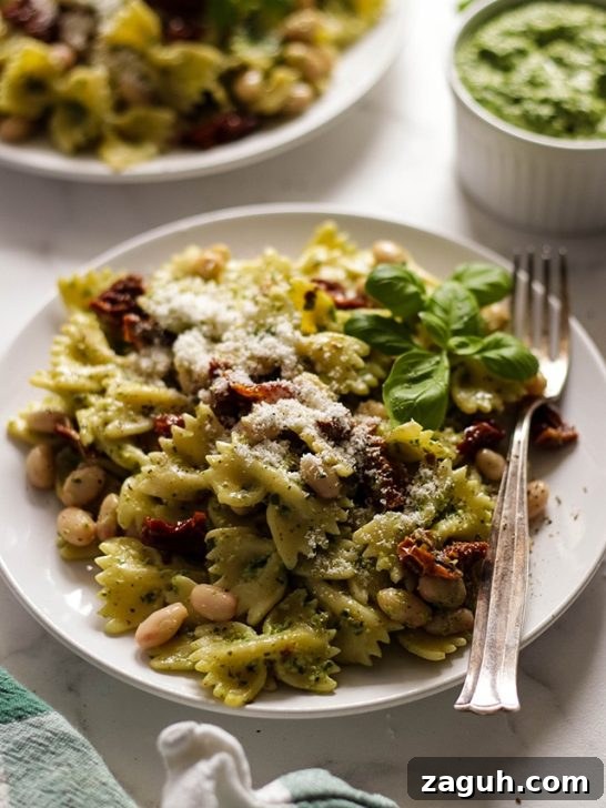 21 Cozy Vegan Comfort Recipes for Every Craving 19 Vegan pesto pasta on a plate next to a bowl of pesto and a cloth napkin