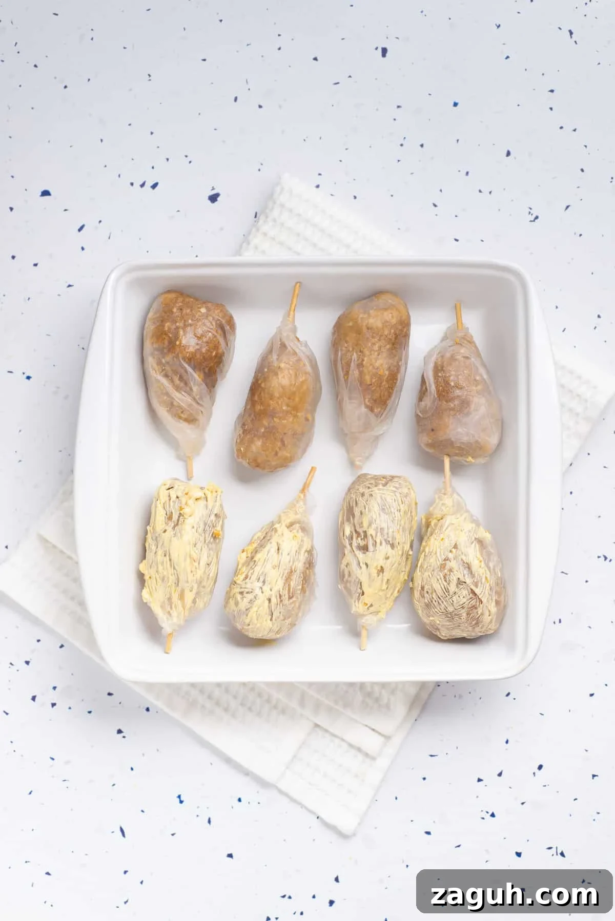 Overhead view of uncooked vegan drumsticks wrapped in rice paper and placed on a white baking dish.