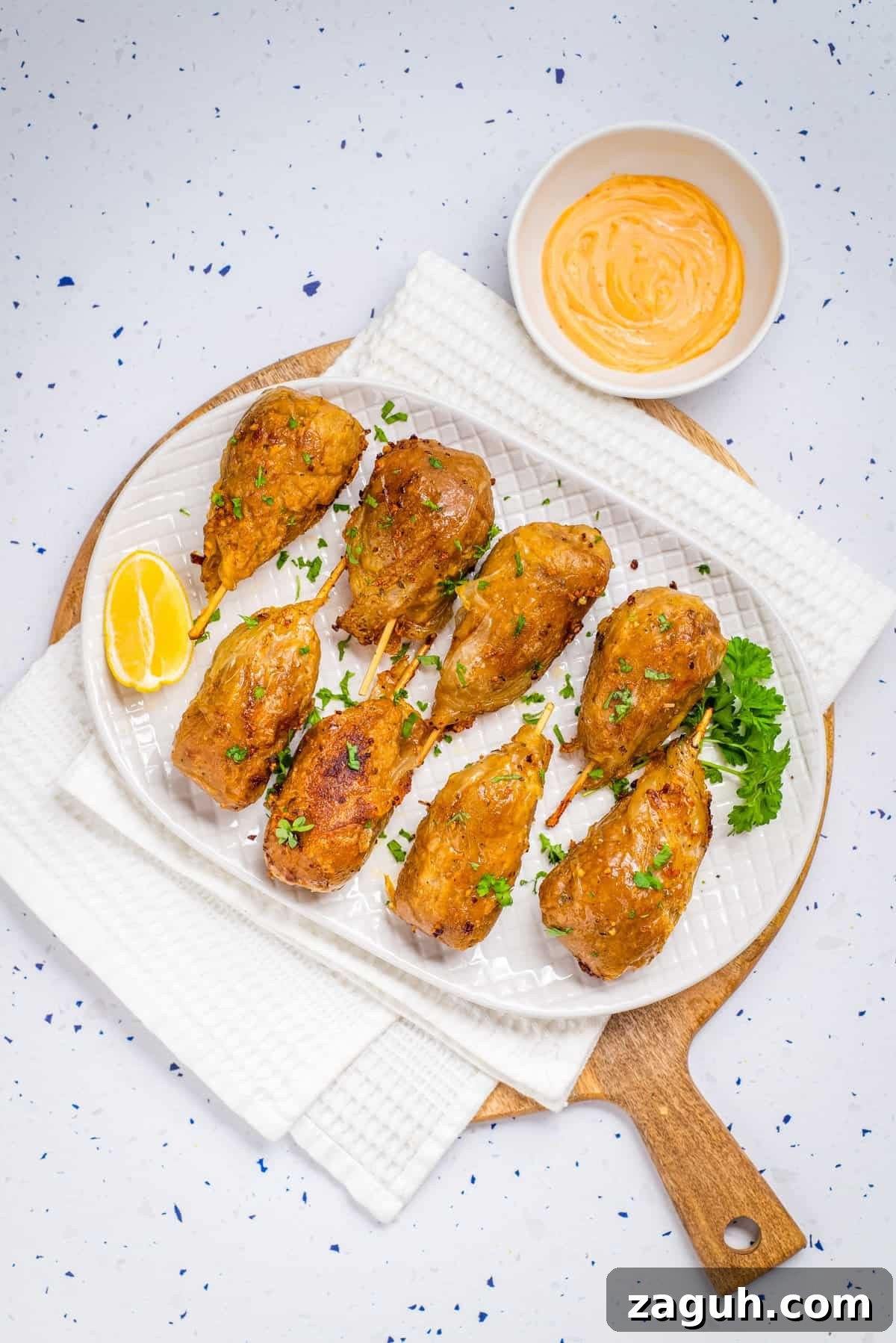 Overhead view of cooked vegan drumsticks on a white plate with sriracha aoili on the side. 