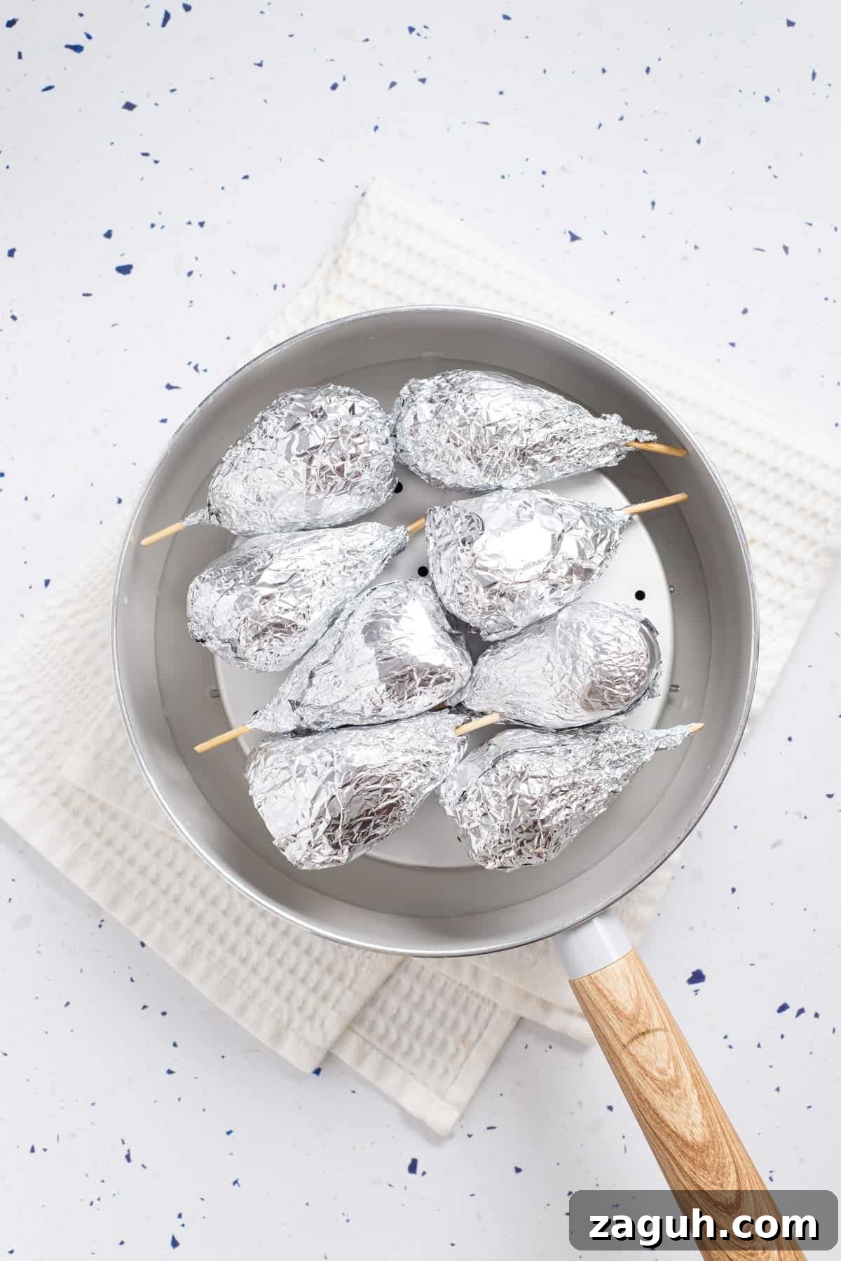 Overhead view of uncooked vegan drumsticks wrapped in foil and placed on a steamer. 