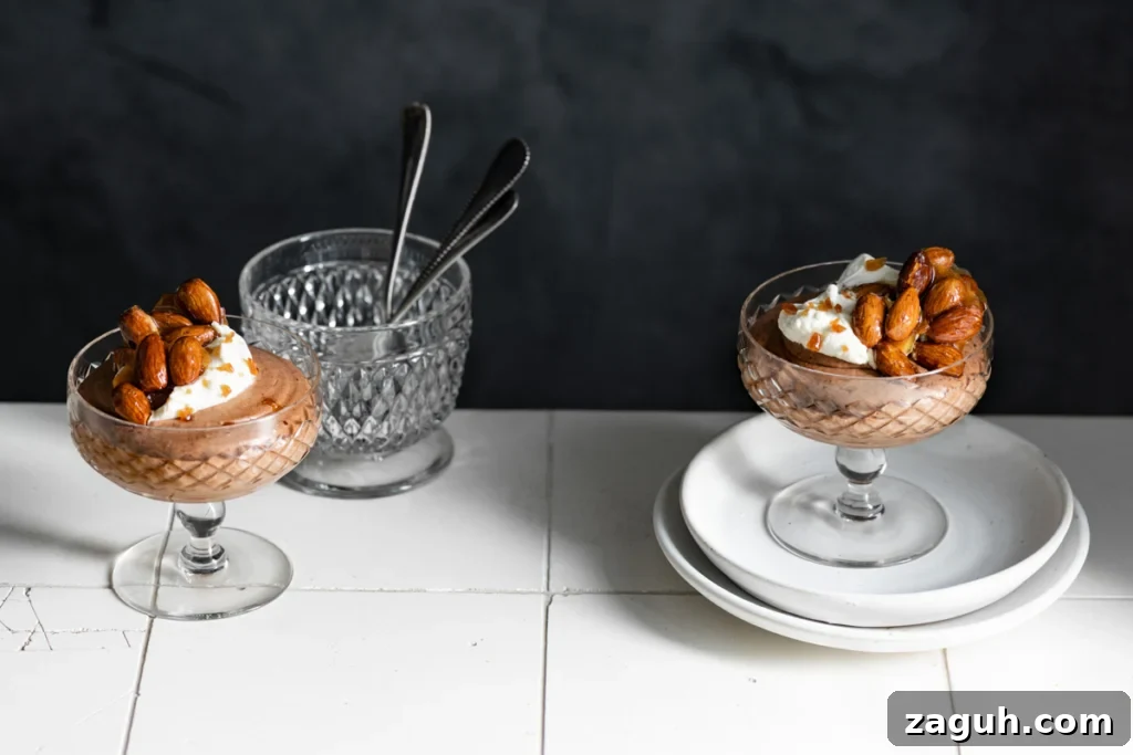 Two glass goblets filled with chocolate mousse and topped with candied nuts on a tile counter.