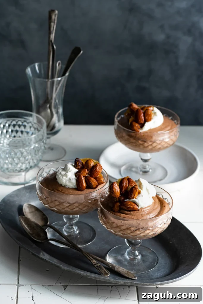 Two glass goblets filled with chocolate mousse and topped with candied nuts on a tile counter.