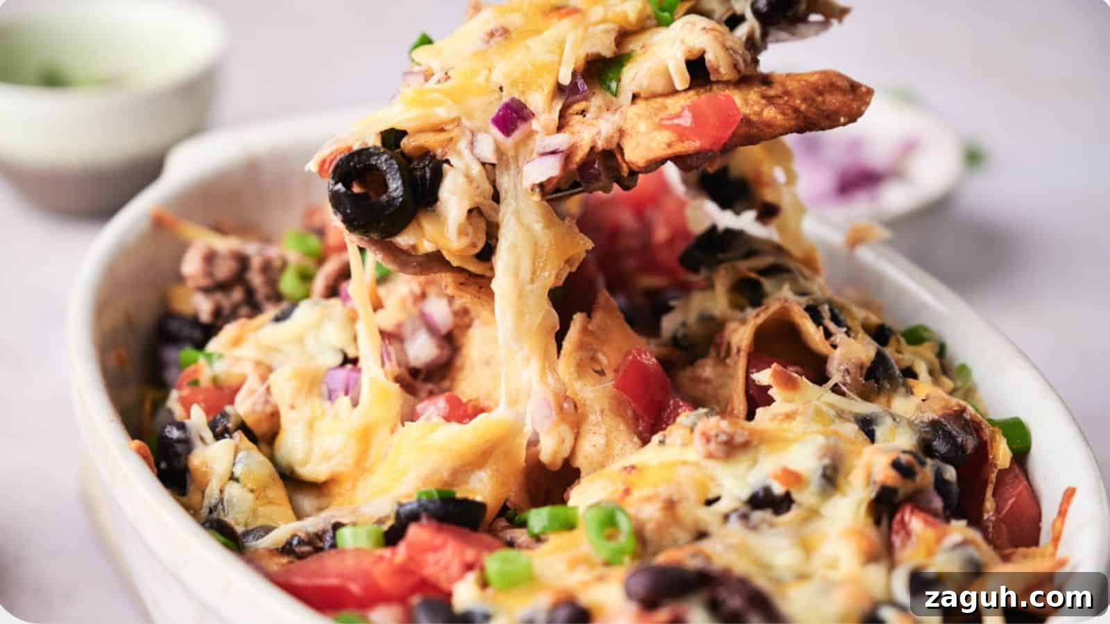 17 Show-Stopping Potluck Recipes That Steal the Spotlight 13 A bowl of taco casserole topped with melted cheese, black olives, tomatoes, and green onions, with a creamy dip in the background.