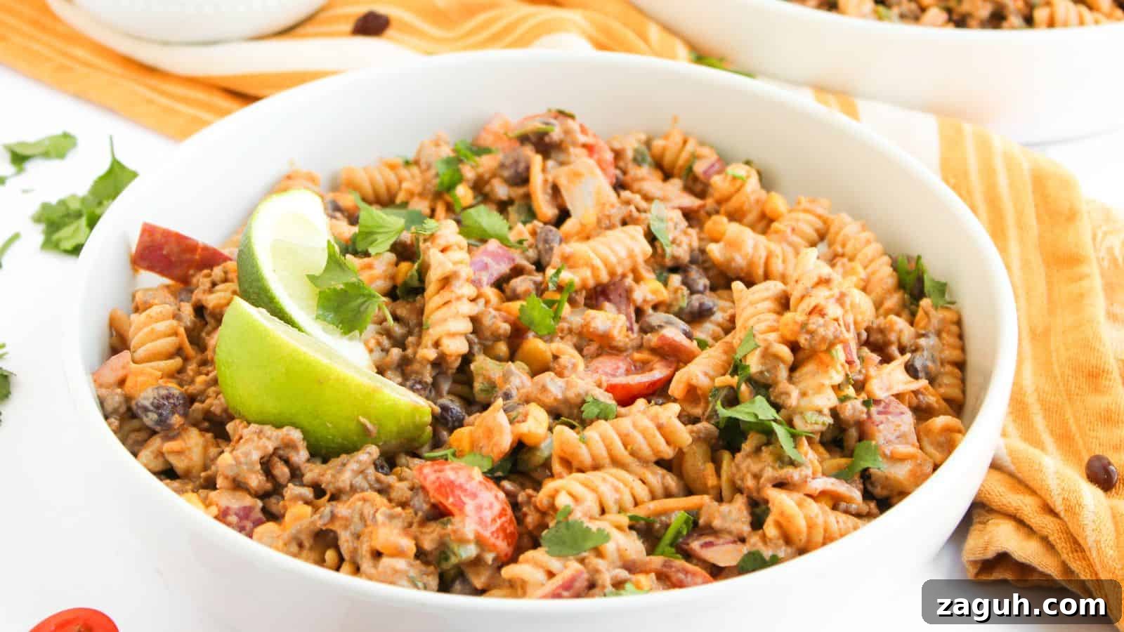 17 Show-Stopping Potluck Recipes That Steal the Spotlight 16 A bowl of fusilli pasta mixed with ground beef, black beans, chopped tomatoes, and herbs, garnished with lime wedges.