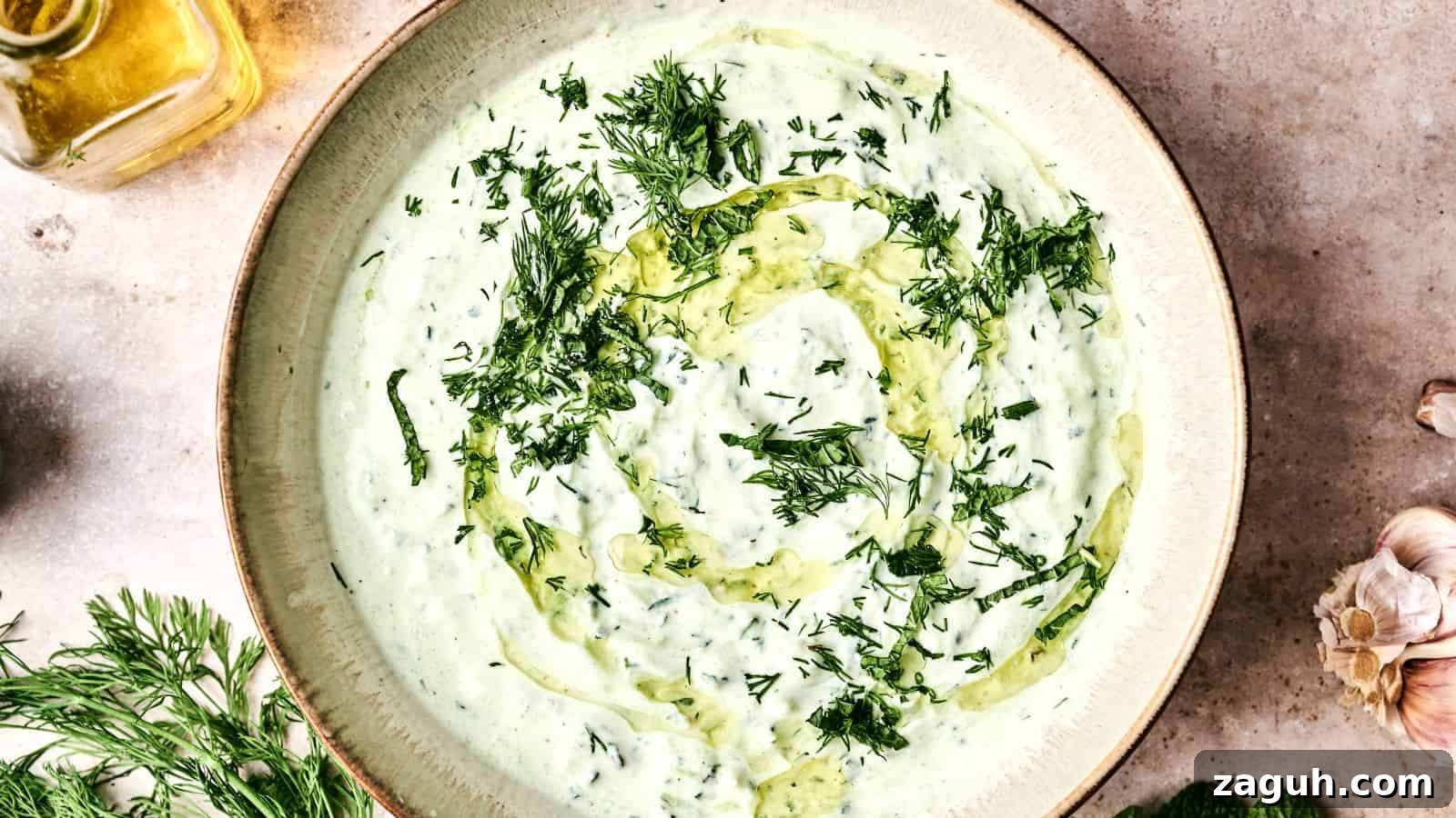 17 Show-Stopping Potluck Recipes That Steal the Spotlight 17 A bowl of creamy tzatziki sauce garnished with chopped dill and a swirl of olive oil. Fresh dill and garlic are nearby.