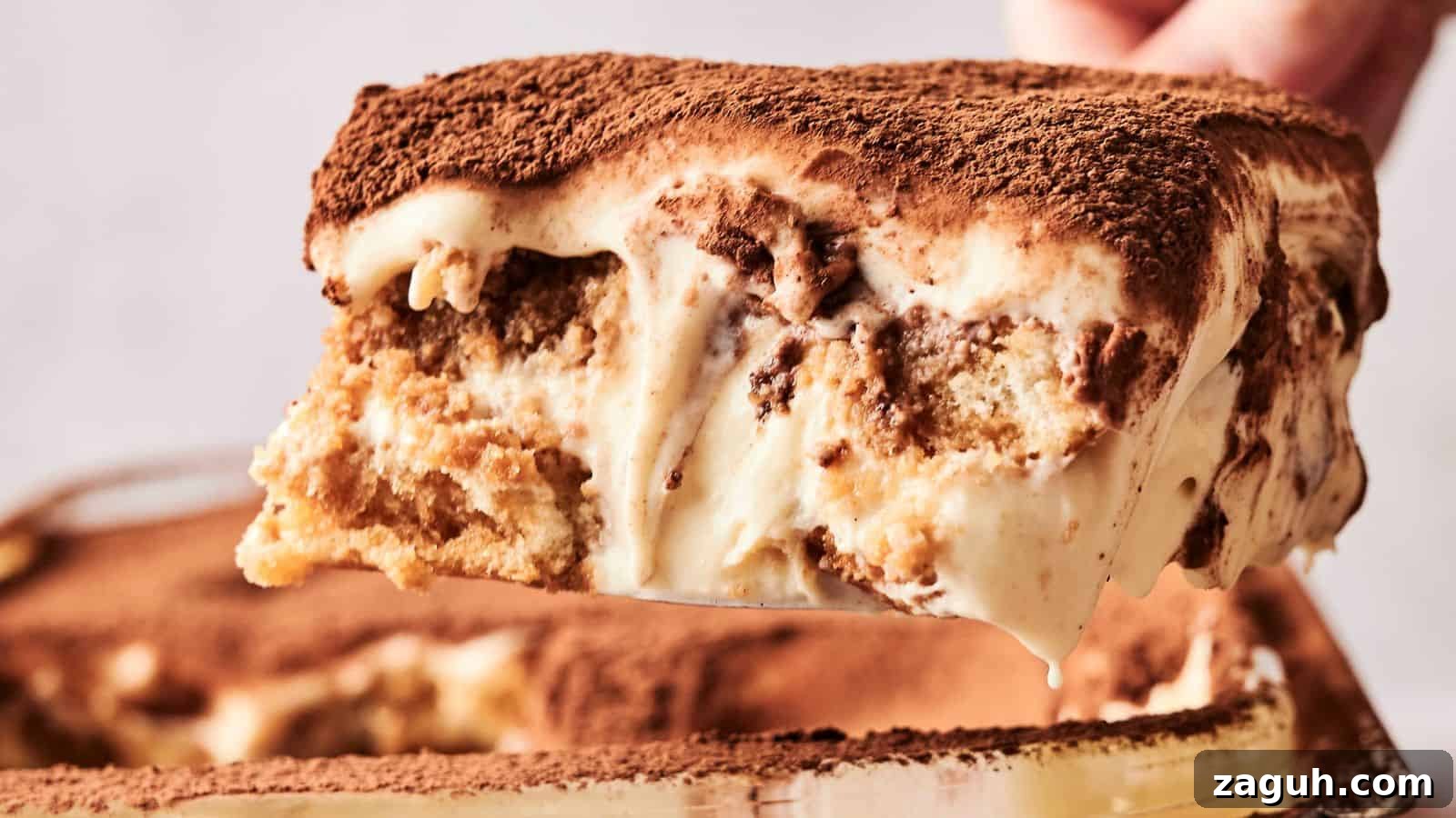 17 Show-Stopping Potluck Recipes That Steal the Spotlight 6 A slice of tiramisu is being lifted from the dish, showcasing layers of coffee-soaked ladyfingers and creamy mascarpone, topped with cocoa powder.