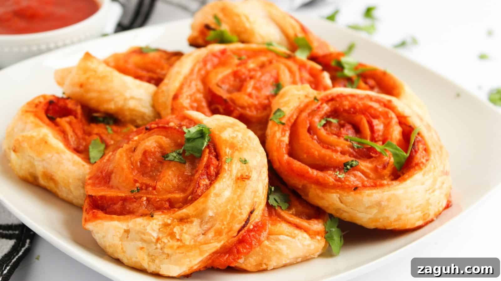 17 Show-Stopping Potluck Recipes That Steal the Spotlight 9 A plate of golden-brown pinwheel pastries filled with tomato sauce and garnished with fresh herbs. A small bowl of sauce is in the background.