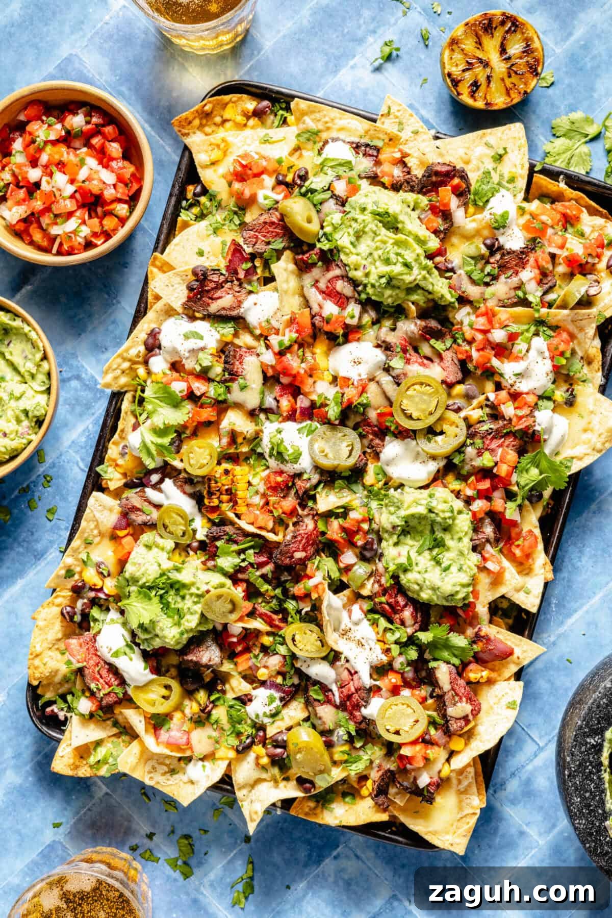 Grilled Chipotle Steak Nachos assembled on sheet pan. Extra sides of pico de gallo and guacamole.