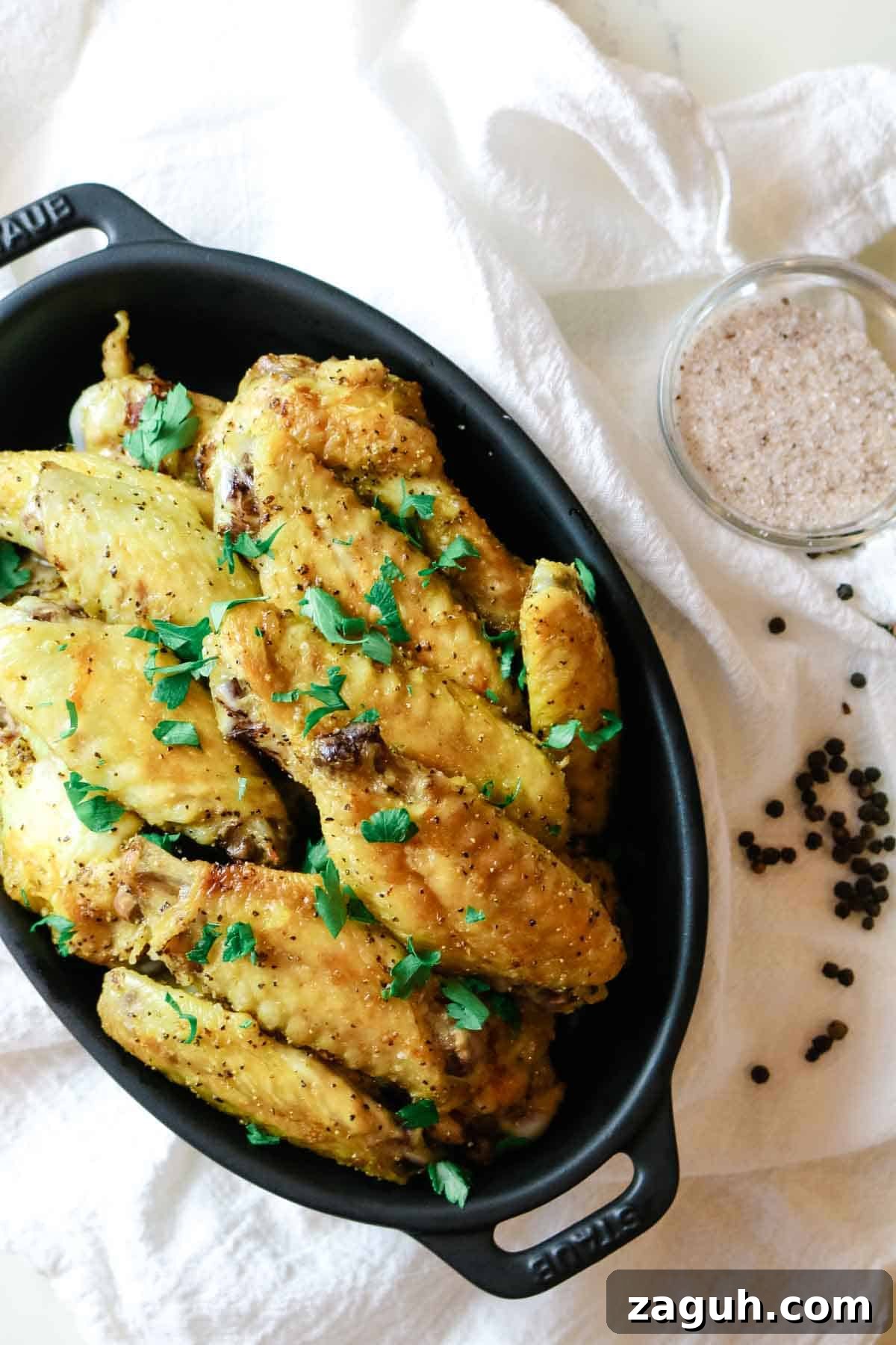 Crispy Baked Salt-and-Pepper Chicken Wings Recipe 2 Chicken wings in a black dish with peppercorns and salt to the side.