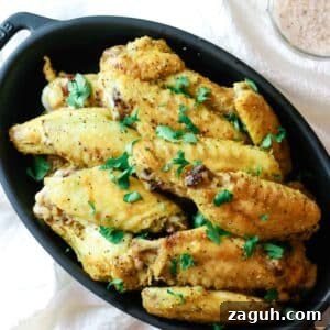 Crispy Baked Salt-and-Pepper Chicken Wings Recipe 11 chicken wings on black dish with green herb.