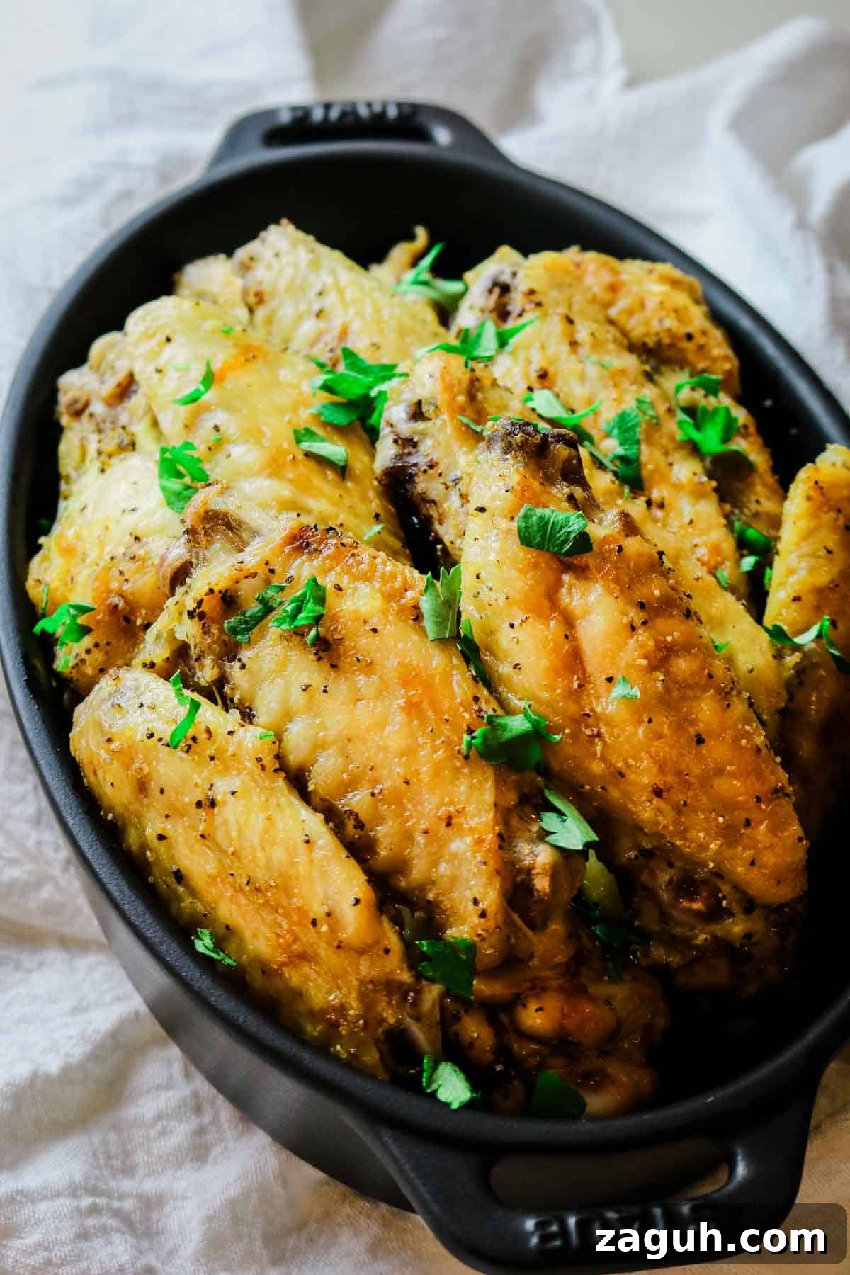 Crispy Baked Salt-and-Pepper Chicken Wings Recipe 4 chicken wings in a black staub dish with parsley garnish.
