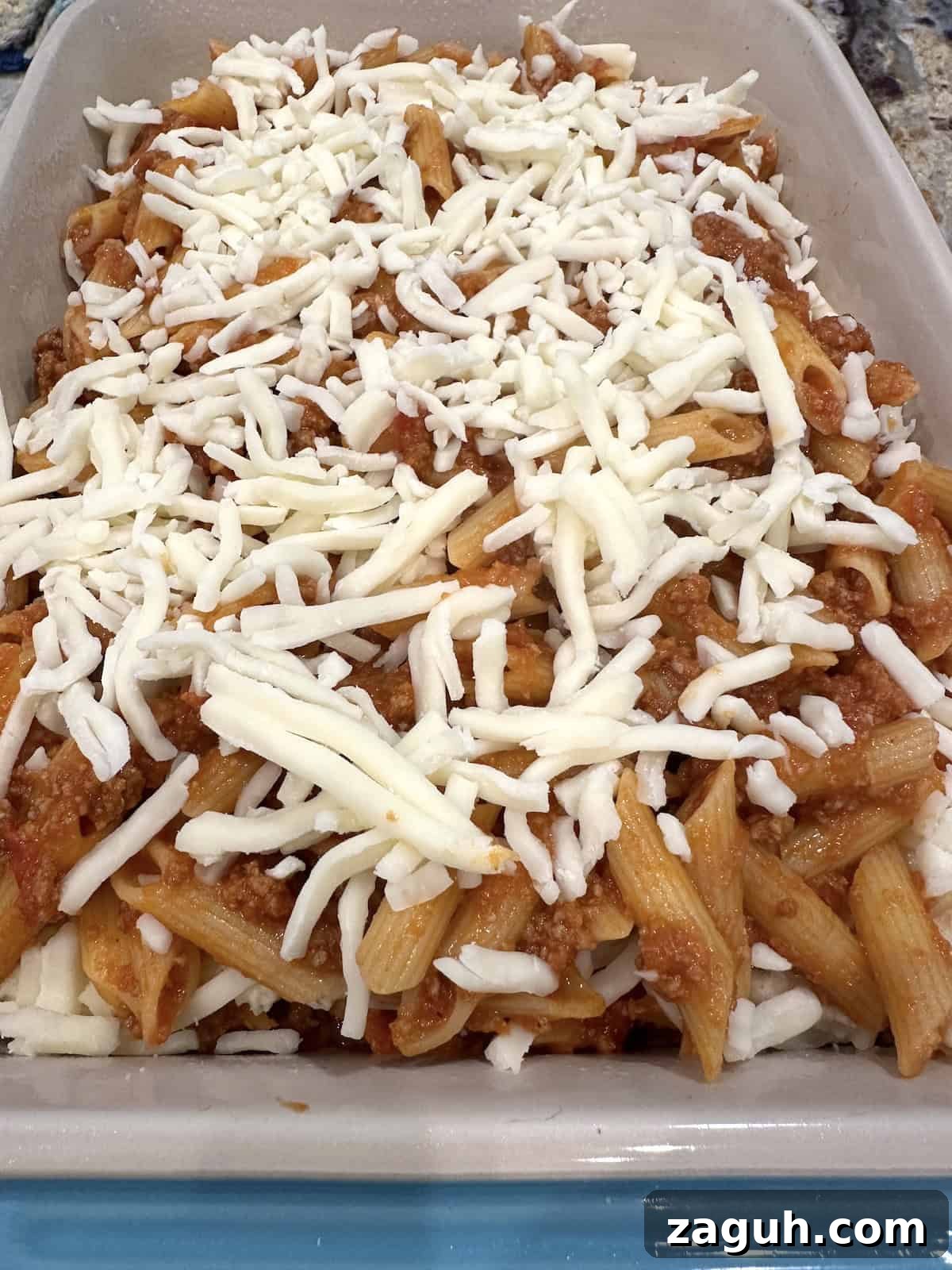 Quick No-Fuss Lasagna Recipe for Busy Weeknights 12 Unbaked pasta, sauce and meat in a baking dish with mozzarella cheese on top.
