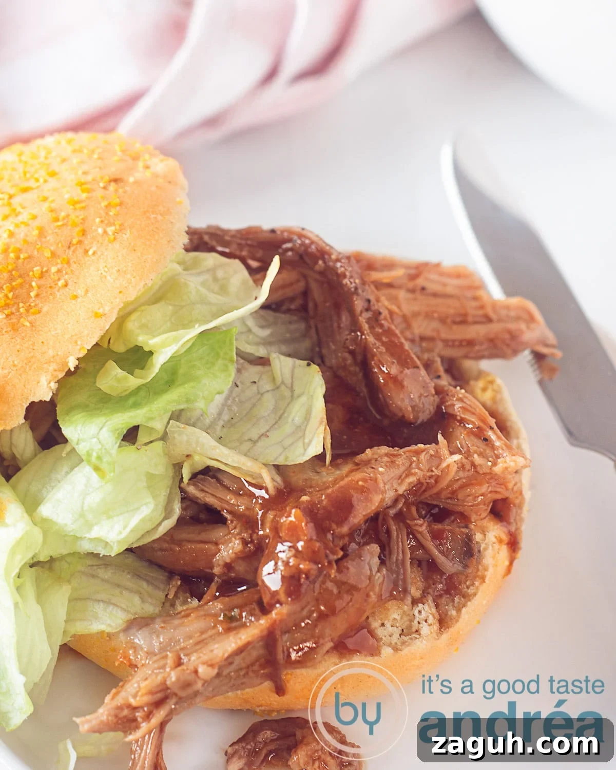 Slow Cooker Pulled Pork Buns Recipe for Tender, Juicy Sandwiches 2 A white background, on top of which a sandwich with BBQ pulled pork and a salad. A knife right next to it, a white background