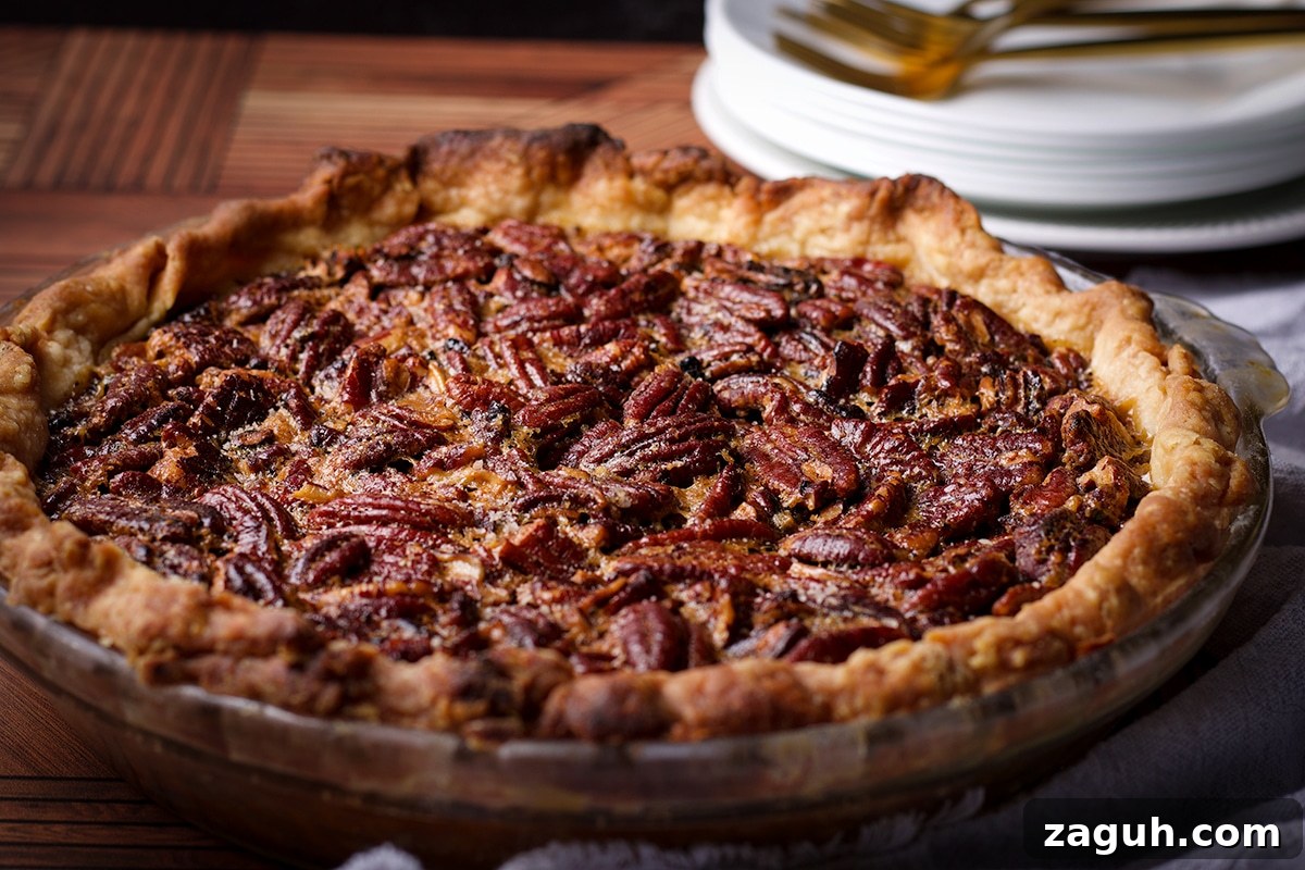 Pecan Pie Made Without Corn Syrup — Classic Recipe with Pure Maple 14 A warm, freshly baked homemade pecan pie resting on a wood table with a stack of plates and forks behind it.