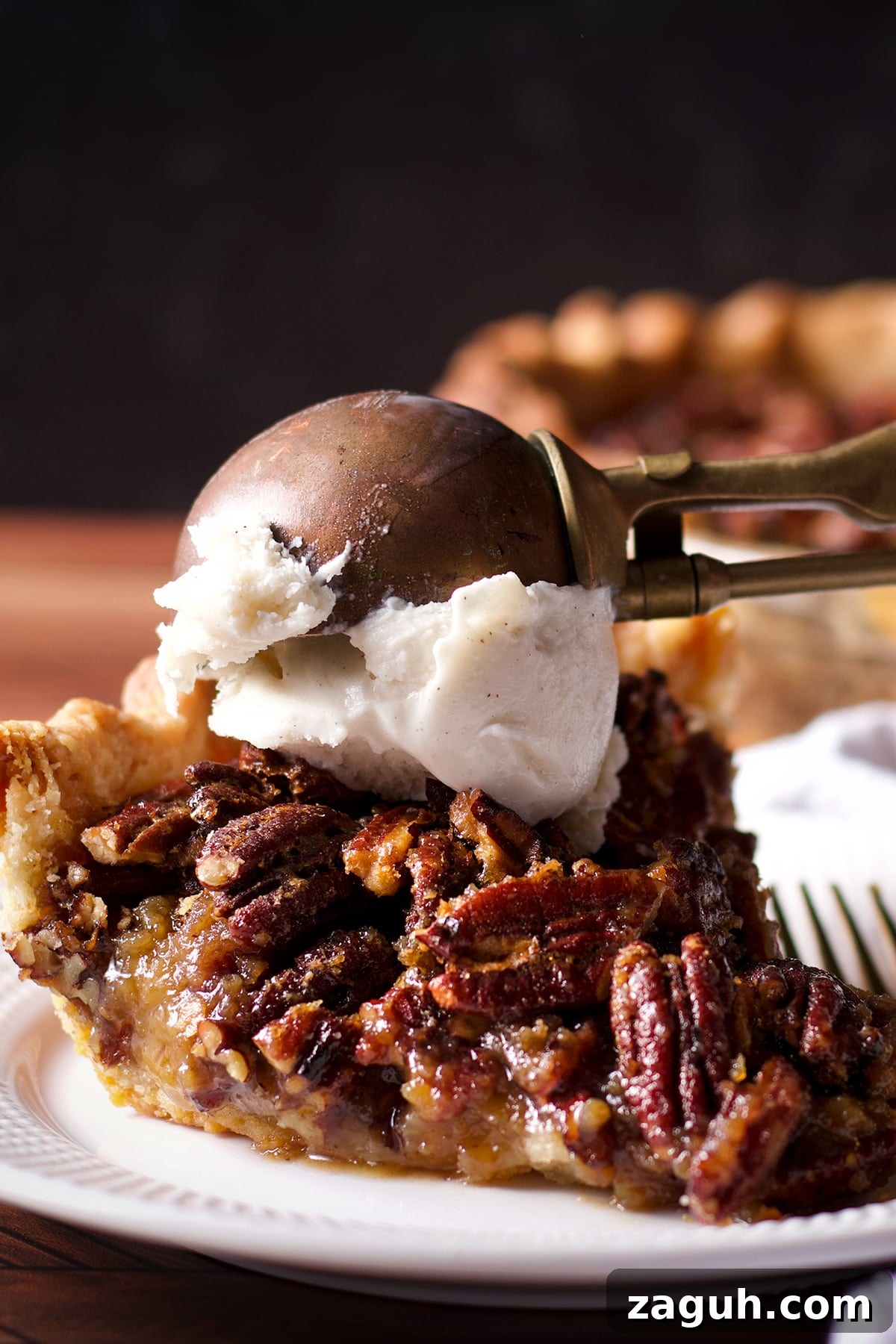 Pecan Pie Made Without Corn Syrup — Classic Recipe with Pure Maple 15 Someone using an old fashioned ice cream scoop to top a slice of pecan pie with vanilla ice cream.