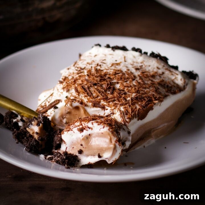 A piece of no-bake chocolate pie on a white plate with a gold fork cutting a bite from the slice.